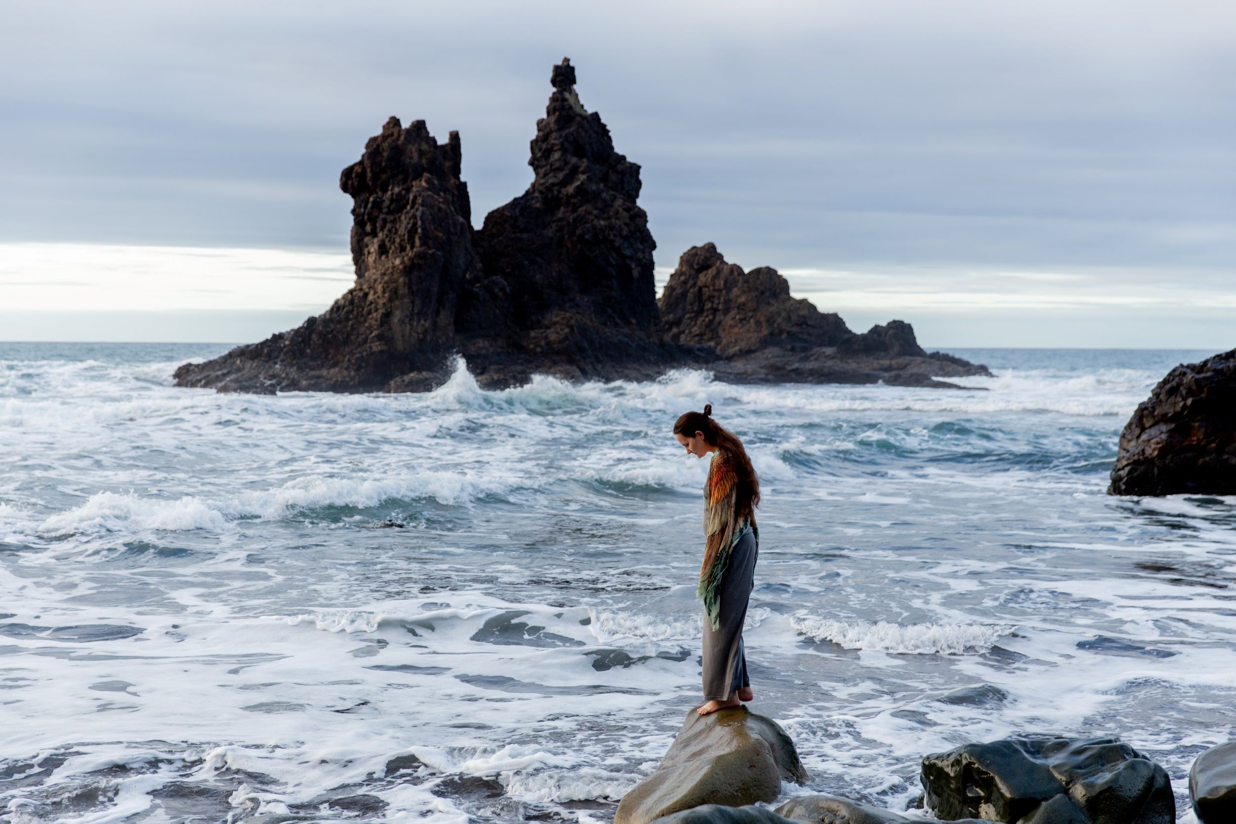 side profile of woman standing on a rock in front of the ocean, looking down into the water
