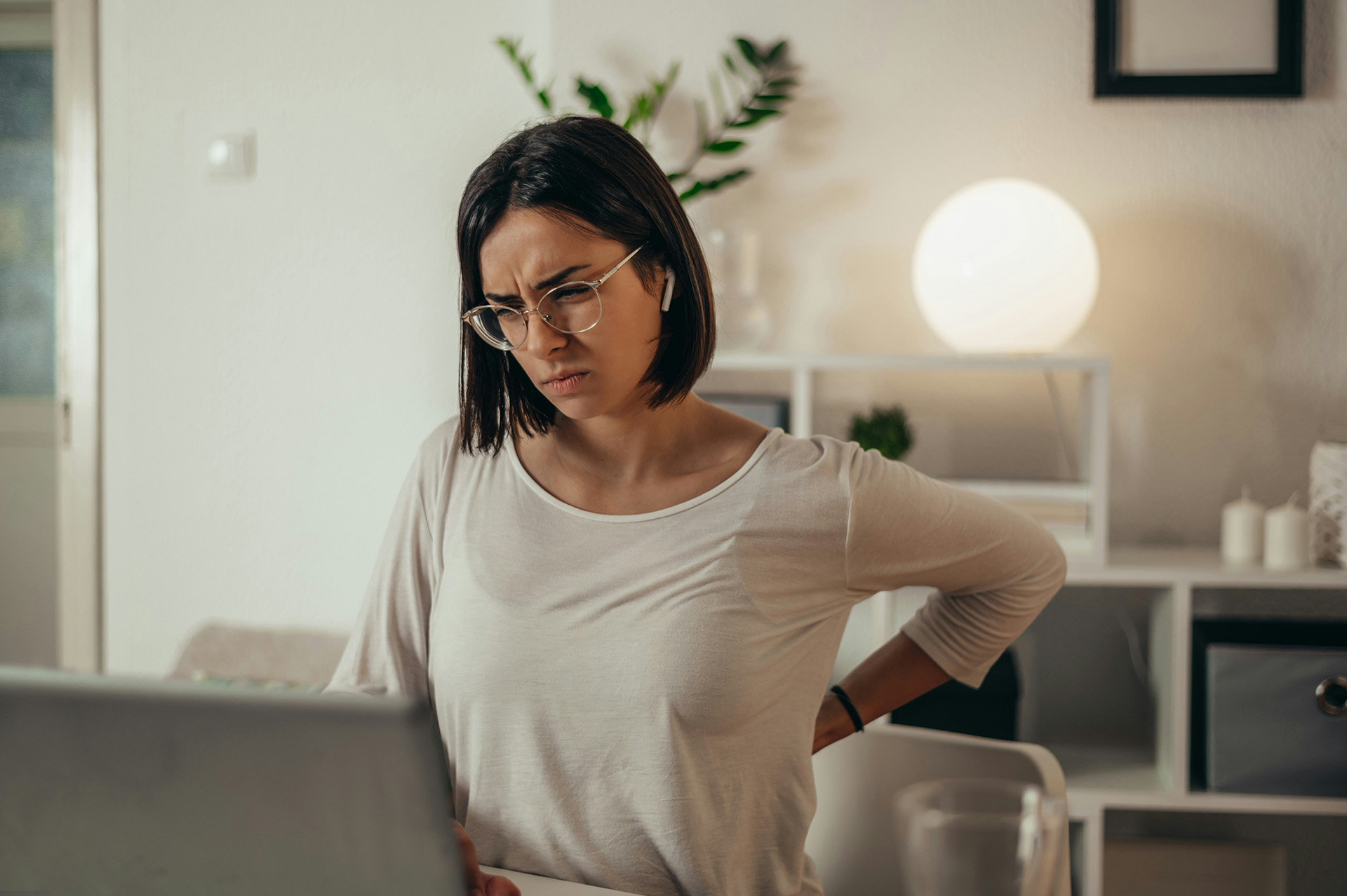 woman sitting at her laptop with her hand on her back looking like she has back pain